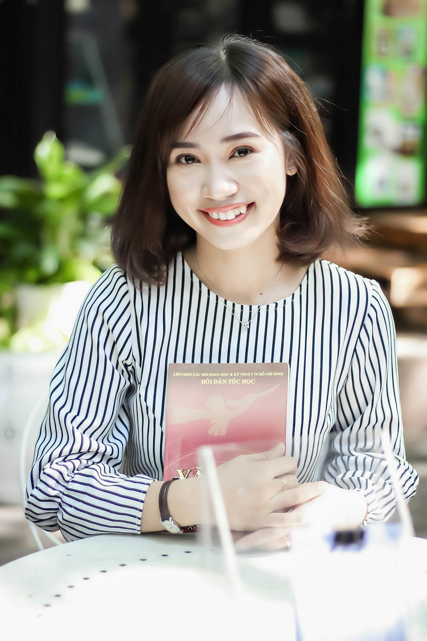 Young woman in striped blouse smiling and holding a book indoors.